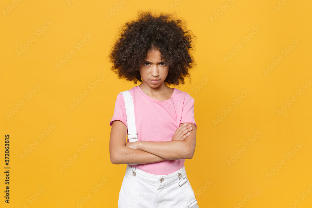 Offended little african american kid girl 12-13 years old in pink t-shirt isolated on yellow background children studio portrait. Childhood lifestyle concept. Mock up copy space. Hold hands crossed. Offended little african american kid girl 12-13 years old in pink t-shirt isolated on yellow background children studio portrait. Childhood lifestyle concept. Mock up copy space. Hold hands crossed.