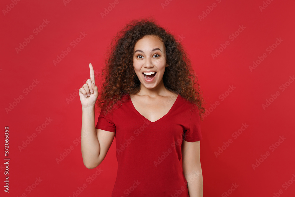 Excited young african american woman girl in casual t-shirt posing isolated on red background studio portrait. People lifestyle concept. Mock up copy space. Hold index finger up with great new idea. Excited young african american woman girl in casual t-shirt posing isolated on red background studio portrait. People lifestyle concept. Mock up copy space. Hold index finger up with great new idea.