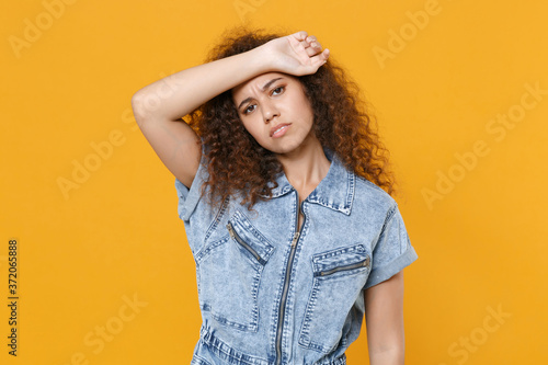 Exhausted tired young african american woman girl in casual denim clothes isolated on yellow wall background studio portrait. People emotions lifestyle concept. Mock up copy space. Put hand on head.