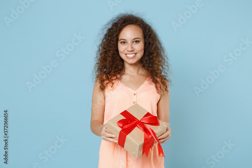 Smiling young african american woman girl in pastel clothes posing isolated on blue background studio. Valentine's Day Women's Day birthday, holiday concept. Hold present box with gift ribbon bow. © ViDi Studio