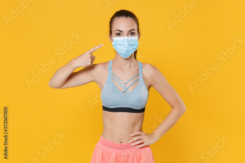 Young fitness sporty woman in sportswear working out isolated on yellow background studio. Workout sport motivation lifestyle concept. Mock up copy space. Pointing index finger on sterile face mask.