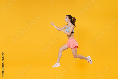 Full length portrait excited fitness woman in sportswear working out isolated on yellow background. Workout sport motivation lifestyle concept. Mock up copy space. Jump, pointing index fingers aside.