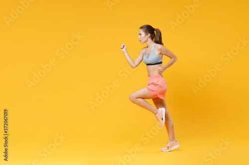 Full length portrait of strong young fitness woman in sportswear working out isolated on yellow background studio portrait. Workout sport motivation lifestyle concept. Mock up copy space. Running.