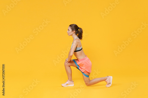 Full length portrait of young fitness sporty woman girl in sportswear working out isolated on yellow background. Workout sport motivation lifestyle concept. Doing exercise lunge with fitness gums.