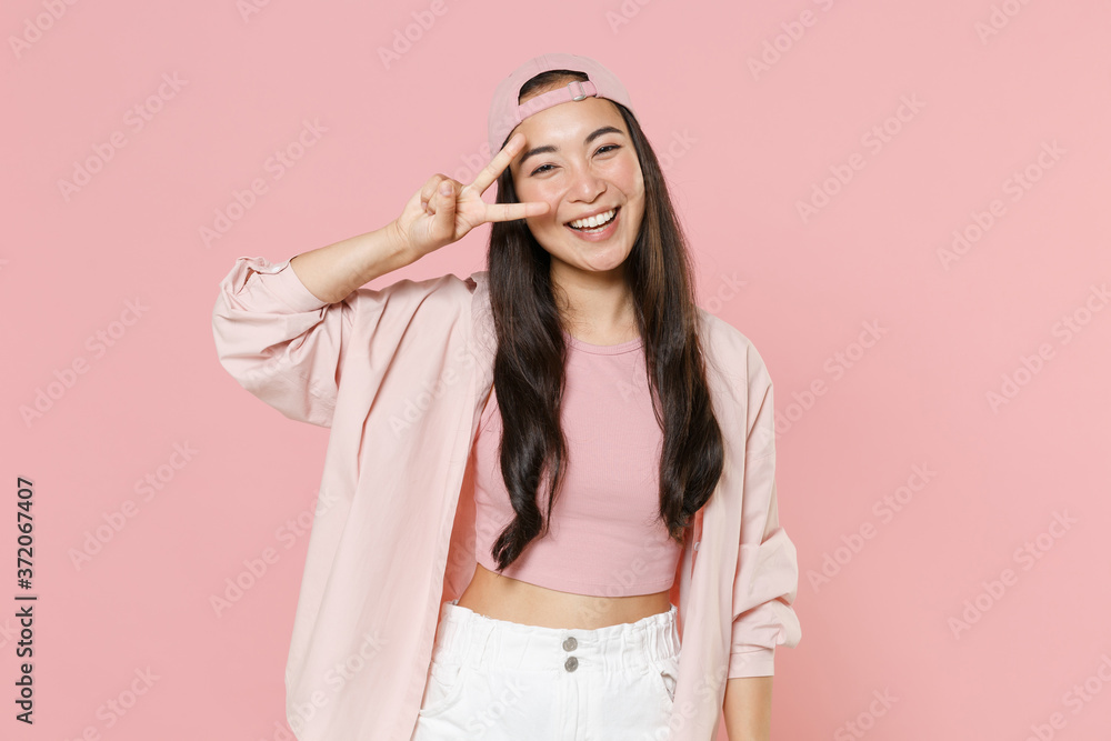 Cheerful young asian woman girl in casual clothes cap posing isolated on pastel pink background studio portrait. People sincere emotions lifestyle concept. Mock up copy space. Showing victory sign. Cheerful young asian woman girl in casual clothes cap posing isolated on pastel pink background studio portrait. People sincere emotions lifestyle concept. Mock up copy space. Showing victory sign.
