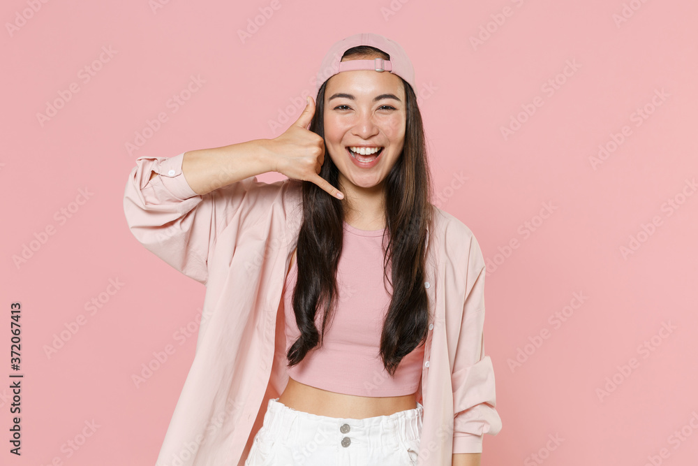 Laughing young asian woman girl in casual clothes cap posing isolated on pastel pink background studio portrait. People lifestyle concept. Mock up copy space. Doing phone gesture says call me back. Laughing young asian woman girl in casual clothes cap posing isolated on pastel pink background studio portrait. People lifestyle concept. Mock up copy space. Doing phone gesture says call me back.