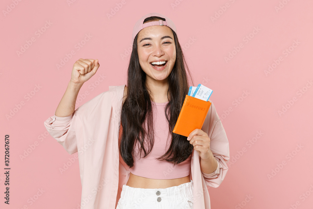 Happy young asian woman in cap isolated on pastel pink background. Passenger traveling abroad to travel on weekends getaway. Air flight journey concept. Hold passport tickets, doing winner gesture.