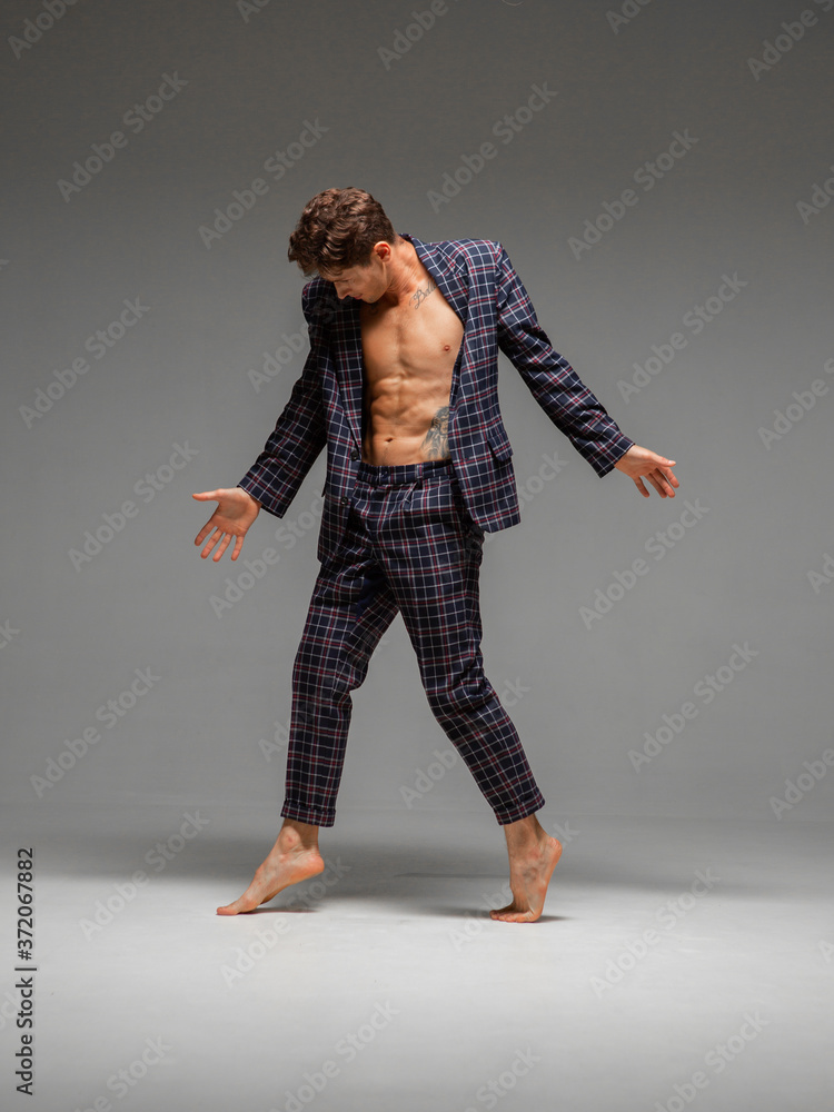 Handsome young guy breakdancer dancing expressive dance in suit with naked torso isolated on gray background