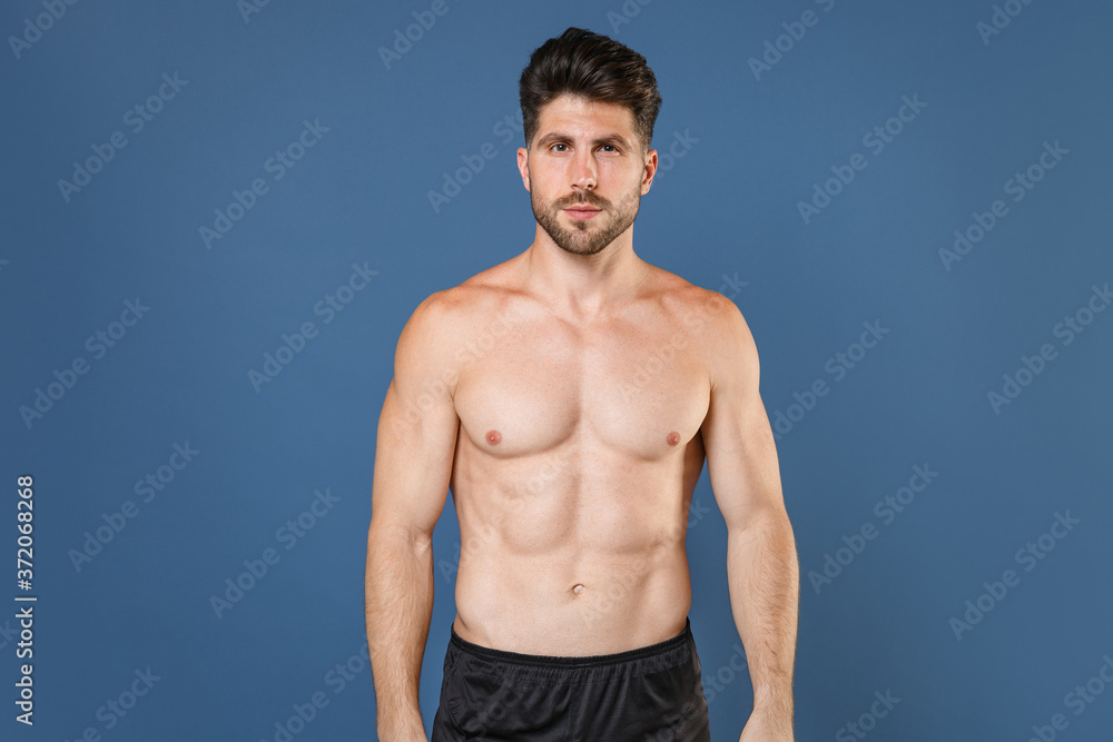 Attractive handsome young bearded fitness sporty strong guy bare-chested muscular sportsman isolated on blue background studio portrait. Workout sport motivation lifestyle concept. Looking camera. Attractive handsome young bearded fitness sporty strong guy bare-chested muscular sportsman isolated on blue background studio portrait. Workout sport motivation lifestyle concept. Looking camera.