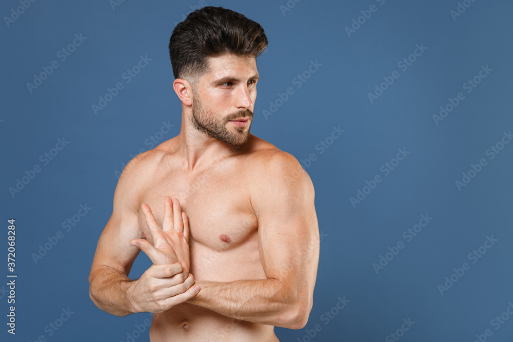 Fototapeta premium Attractive young bearded fitness sporty strong guy bare-chested muscular sportsman isolated on blue background studio portrait. Workout sport motivation lifestyle concept. Doing stretching exercising.