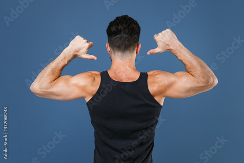Back rear view of young fitness sporty strong guy sportsman in black undershirt isolated on blue background studio portrait. Workout sport motivation lifestyle concept. Pointing thumbs on himself.