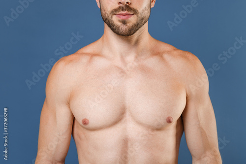 Cropped image of young bearded fitness sporty strong guy bare-chested muscular sportsman posing isolated on blue wall background studio portrait. Workout sport motivation lifestyle concept.