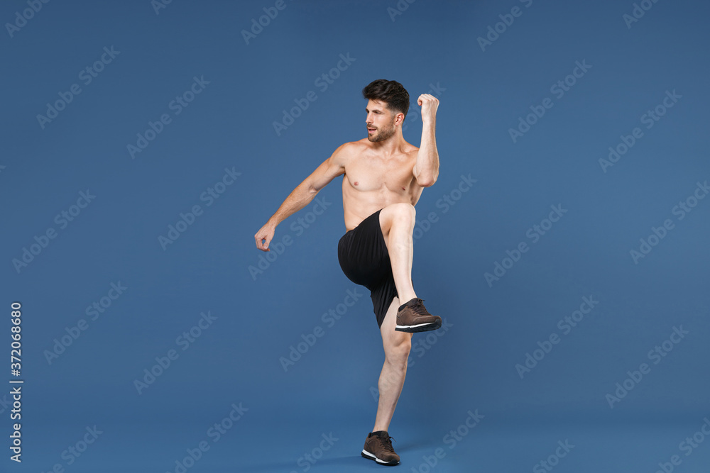 Full length portrait of young fitness sporty strong guy bare-chested muscular sportsman isolated on blue background. Workout sport motivation lifestyle concept. Doing stretching exercising for legs.