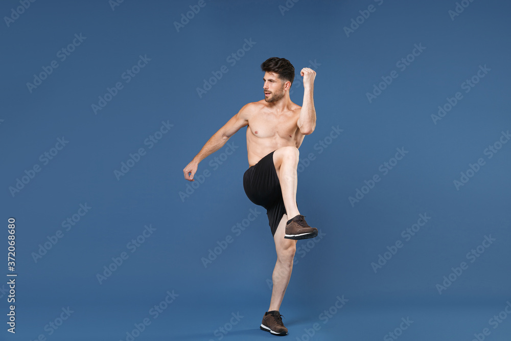 Full length portrait of young fitness sporty strong guy bare-chested muscular sportsman isolated on blue background. Workout sport motivation lifestyle concept. Doing stretching exercising for legs. Full length portrait of young fitness sporty strong guy bare-chested muscular sportsman isolated on blue background. Workout sport motivation lifestyle concept. Doing stretching exercising for legs.