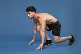 Full length portrait side view of young bearded fitness sporty strong guy bare-chested muscular sportsman isolated on blue background. Workout sport motivation lifestyle concept. Getting ready to run.