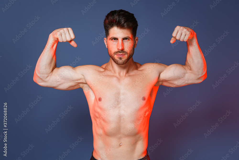 Attractive young bearded fitness sporty strong guy bare-chested muscular sportsman isolated on blue background studio portrait. Workout sport motivation lifestyle concept. Showing biceps, muscles. Attractive young bearded fitness sporty strong guy bare-chested muscular sportsman isolated on blue background studio portrait. Workout sport motivation lifestyle concept. Showing biceps, muscles.