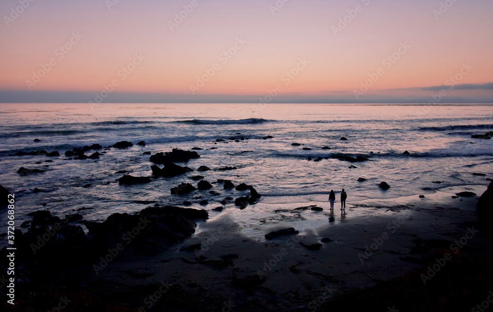 a young couple is dwarfed by the seascape as they look toward the sunset