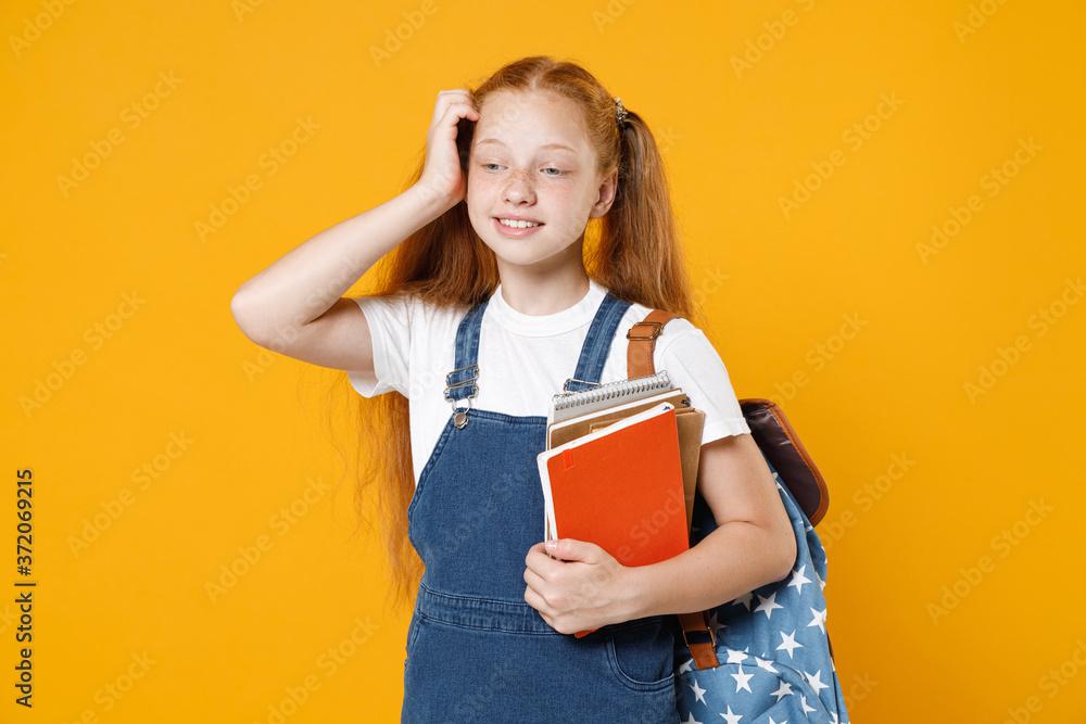 Young redhead girl 12-13 years old in white t-shirt denim uniform backpack hold school textbook notebook book isolated on yellow background children studio portrait Kids education lifestyle concept Young redhead girl 12-13 years old in white t-shirt denim uniform backpack hold school textbook notebook book isolated on yellow background children studio portrait Kids education lifestyle concept