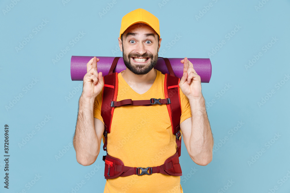 Traveler man in cap with backpack isolated on blue background. Tourist traveling on weekend getaway. Tourism discovering hiking concept. Waiting for special moment keeping fingers crossed making wish. Traveler man in cap with backpack isolated on blue background. Tourist traveling on weekend getaway. Tourism discovering hiking concept. Waiting for special moment keeping fingers crossed making wish.