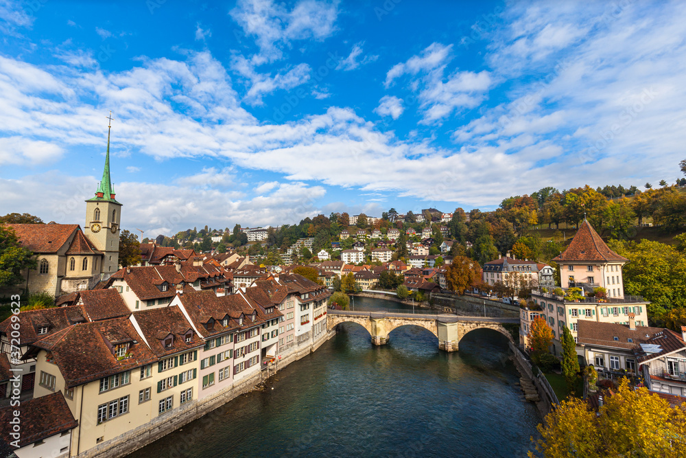 Beautiful view of Bern old town and Aare river from Nydeggbrücke bridge with Nydeggkirche church and Untertorbrücke, on sunny autumn day with blue sky and cloud, Switzerland