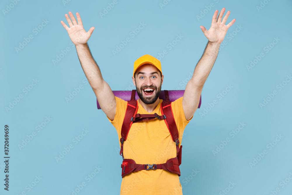 Excited traveler young man in yellow casual t-shirt, cap with backpack isolated on blue background. Tourist traveling on weekend getaway. Tourism discovering hiking concept. Spreading rising hands. Excited traveler young man in yellow casual t-shirt, cap with backpack isolated on blue background. Tourist traveling on weekend getaway. Tourism discovering hiking concept. Spreading rising hands.