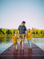Cool baby boys with mother holding hands go on pier. Summer photography for blog or ad about family and travel