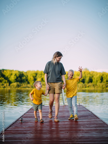 Cool baby boys with mother holding hands go on pier. Summer photography for blog or ad about family and travel