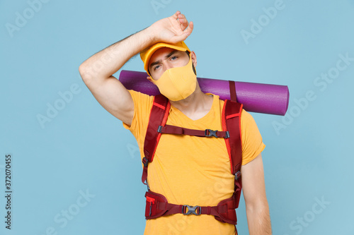Tired traveler young man in yellow casual t-shirt face mask cap with backpack isolated on blue background. Tourist traveling on weekend getaway. Tourism discovering hiking concept. Put hand on head.
