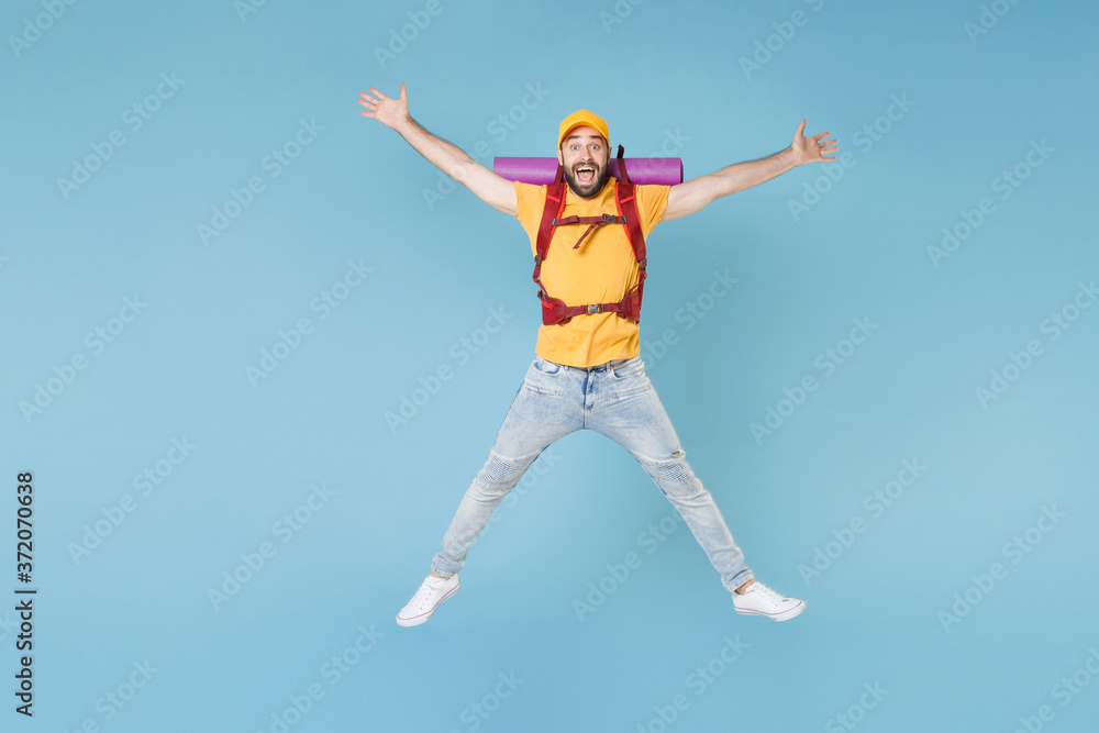 Full length portrait funny young traveler man in t-shirt cap backpack isolated on blue background. Tourist traveling on weekend getaway. Tourism discovering hiking concept. Jump spreading hands legs.