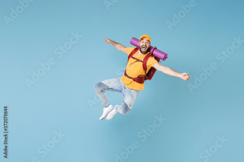 Full length portrait Excited young traveler man in t-shirt cap backpack isolated on blue background. Tourist traveling on weekend getaway. Tourism discovering hiking concept. Jumping spreading hands.