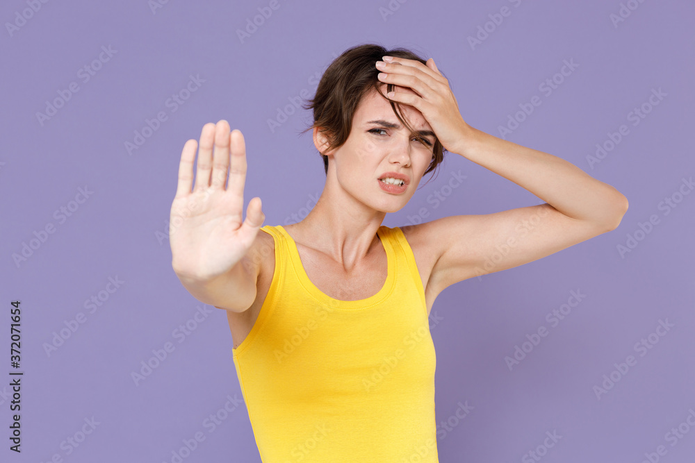 Tired young brunette woman girl in yellow casual tank top posing isolated on pastel violet wall background studio portrait. People lifestyle concept. Showing stop gesture with palm, put hand on head. Tired young brunette woman girl in yellow casual tank top posing isolated on pastel violet wall background studio portrait. People lifestyle concept. Showing stop gesture with palm, put hand on head.