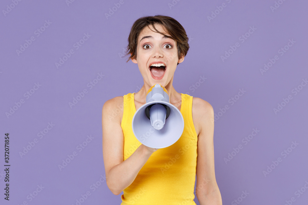 Surprised young brunette woman girl wearing yellow casual tank top posing isolated on pastel violet wall background studio portrait. People sincere emotions lifestyle concept. Screaming in megaphone. Surprised young brunette woman girl wearing yellow casual tank top posing isolated on pastel violet wall background studio portrait. People sincere emotions lifestyle concept. Screaming in megaphone.