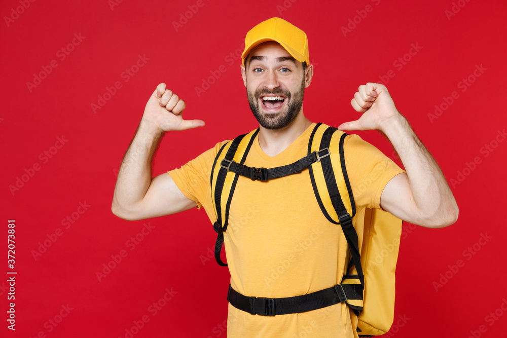 Delivery employee man guy male 20s in yellow cap t-shirt uniform thermal bag backpack with food work as courier isolated on red background studio. Service during quarantine coronavirus covid-19 virus.