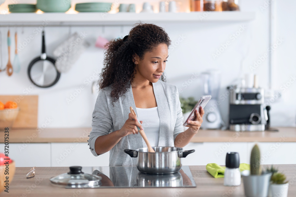 Confident young african american woman healthy food while using her mobile phone in the kitchen at home. Confident young african american woman healthy food while using her mobile phone in the kitchen at home.