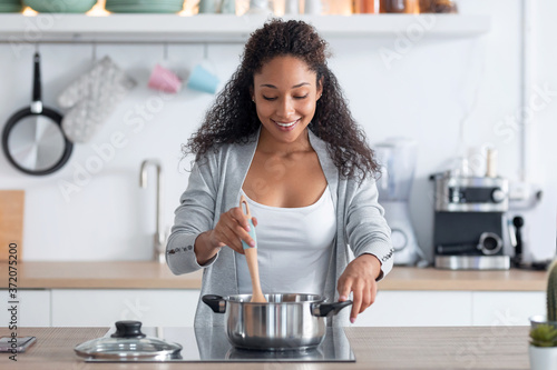 Fotografie Happy young african american woman cooking healthy food in casserole in the kitchen at home
