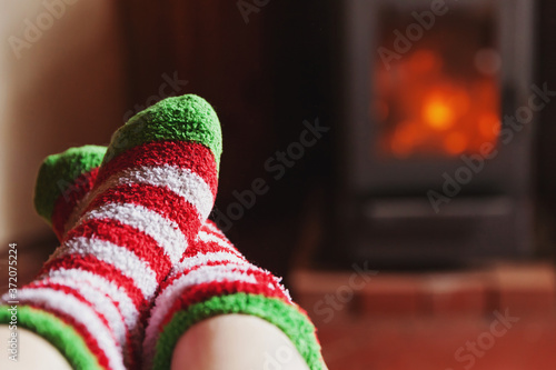 Feet legs in winter clothes wool socks at fireplace background. Woman sitting at home on winter or autumn evening relaxing and warming up. Winter and cold weather concept. Hygge Christmas eve.