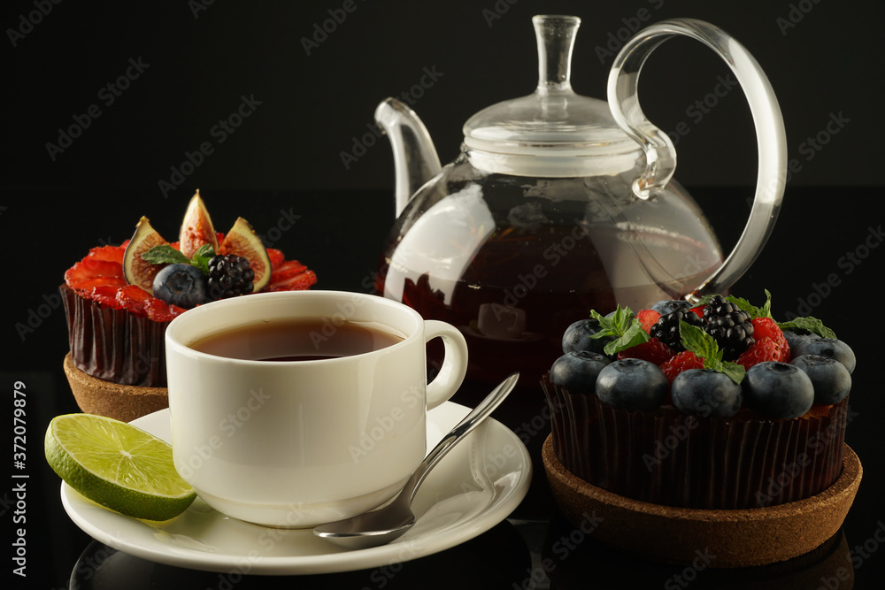 black tea with lime and cake in a tartlet with berries and fruits. Ripe strawberries, juicy blackberries, sweet blueberries and figs with mint on a dark background. black tea with lime and cake in a tartlet with berries and fruits. Ripe strawberries, juicy blackberries, sweet blueberries and figs with mint on a dark background.