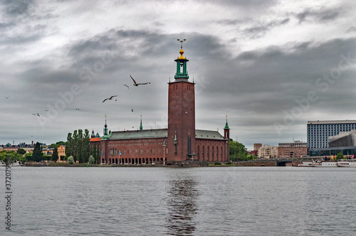 A group of seagulls hover over the cold waters of the northern seas against the backdrop of ancient buildings and overcast skies on a cool summer day