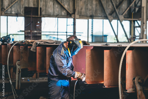 a worker with a mask does electric welding of steel in a shipyard