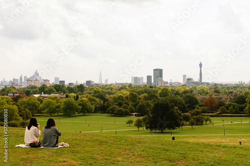 Primrose Hill in London with people sitting on grass. City skyline in haze.