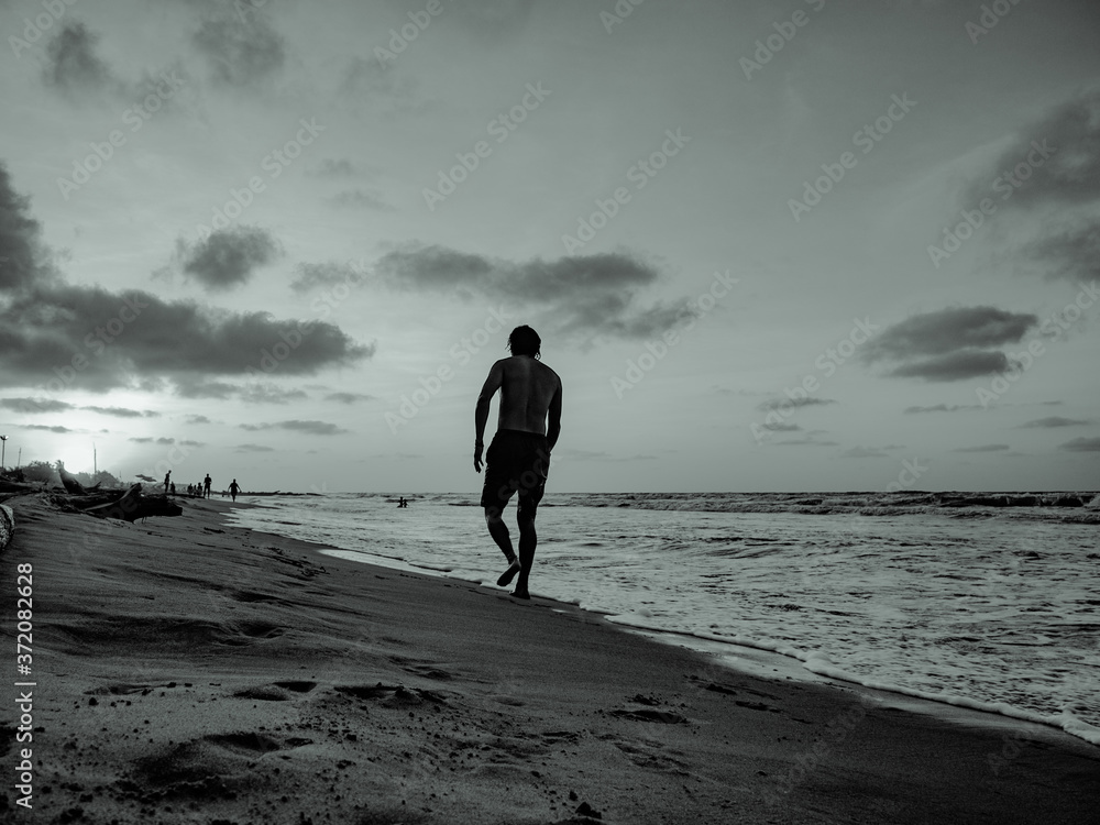 man alone walking on the beach in black and white at sunset  