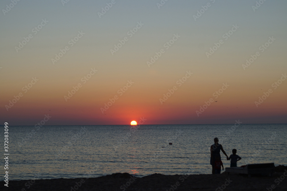 silhouettes of people standing alone on a deserted beach and admiring the sunset on the sea