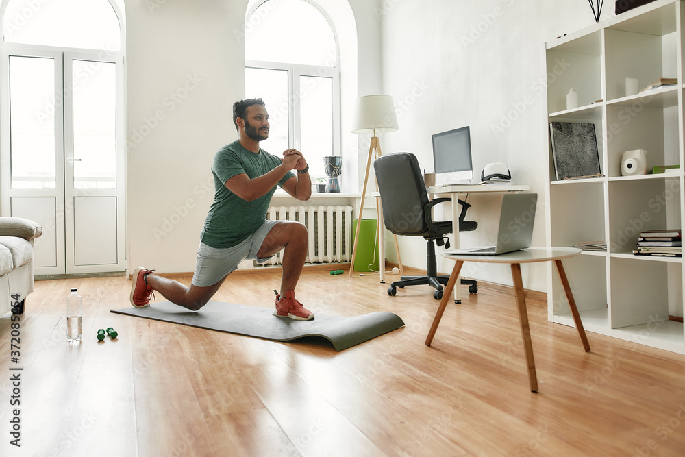 Fototapeta premium Fitness matters. Young active man showing exercises while streaming, broadcasting video lesson on training at home using laptop. Sport, online gym concept