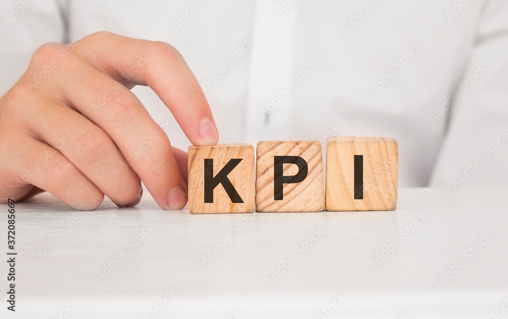 Naklejka premium Close up young man's hand in white shirt wooden block cube for Kpi wording on white marble table floor