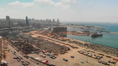 Aftermath of the Beirut port explosion, featuring a damaged grain silo, twisted metal structures, and scattered debris amid ongoing reconstruction efforts.