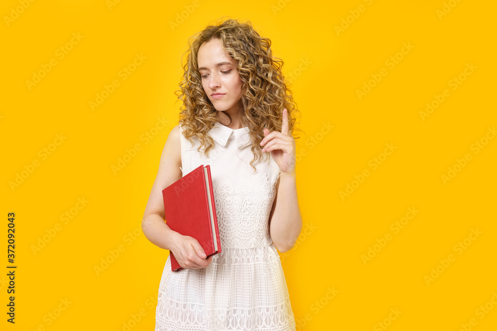 Portrait of a young smiling woman who holds a book in her hands and points her finger to the side. Female portrait. Portrait of a young smiling woman who holds a book in her hands and points her finger to the side. Female portrait.