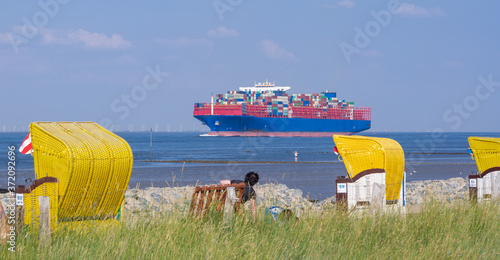 Strandkörbe am Strand von Altenbruch bei Cuxhaven vor einem großen Containerschiff auf der Elbe. photo