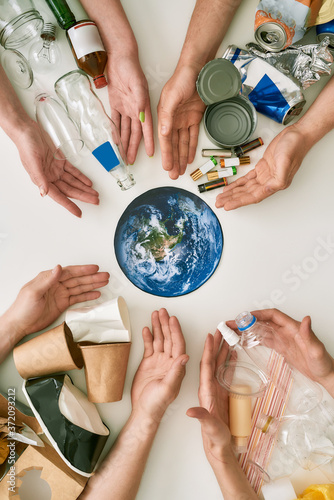 Conceptual flat lay with many hands and different waste, garbage types reaching planet Earth made of paper in the center over white background photo