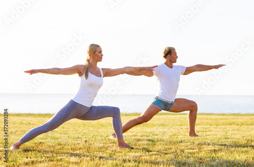 Fit man and beautiful woman practicing yoga outdoor on the grass. Stretching exercise in the sunset. Sport, fitness, health care and lifestyle concepts.