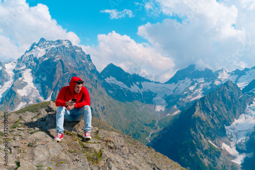 Adult male in red hoodie with hood enjoying beautiful view in mountainous area. © Anton Dios